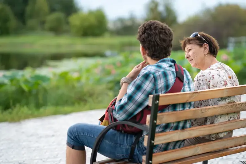 Jongere en begeleider in gesprek op een bankje in het groen