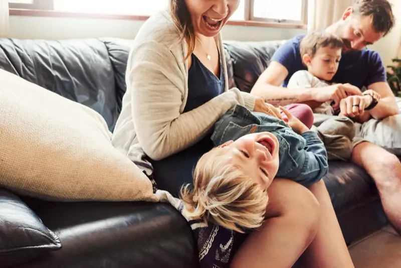 Moeder die lachend met haar kinderen op de bank speelt